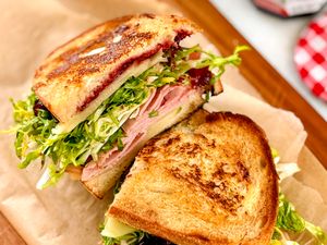 Slices of a sandwich with ham cheese lettuce and jam on toasted bread arranged on parchment paper