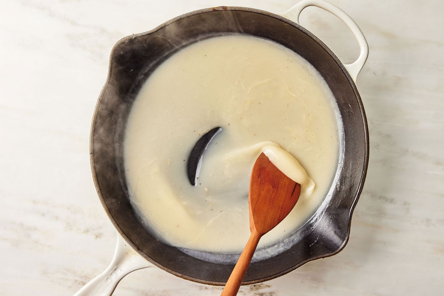 sauce thickening on a skillet, wooden spatula stirring it for Chicken Francese recipe