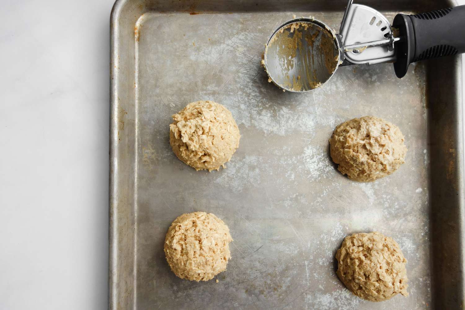 Scoops of Chewy Peanut Butter Oatmeal Cookies and a Cookie Scoop on a Baking Sheet 