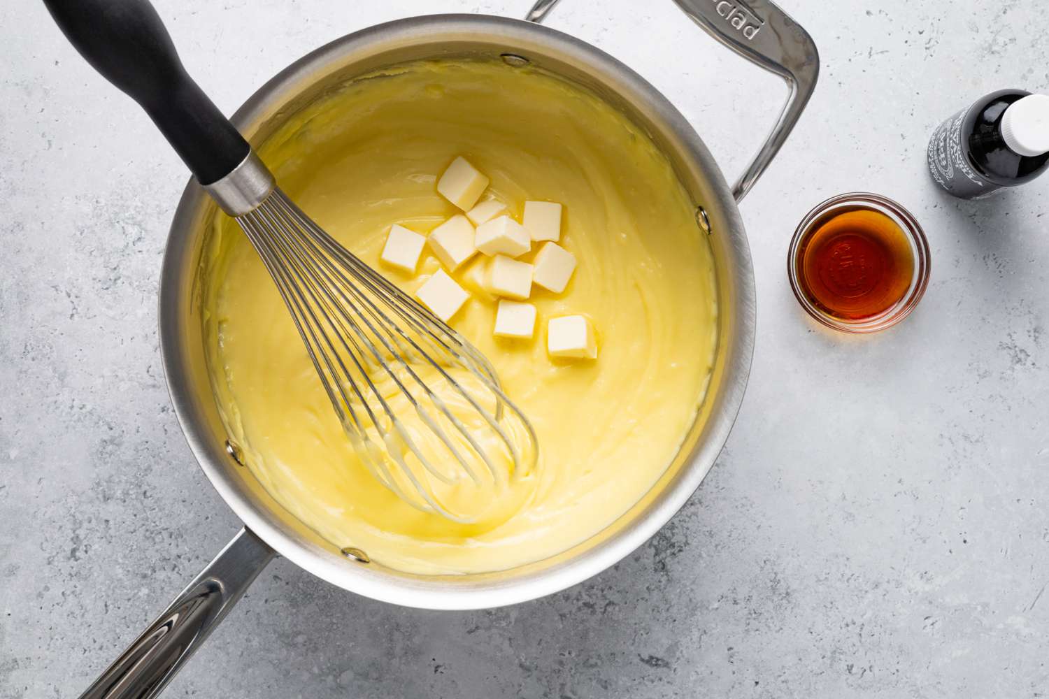 Butter in Pot of Vanilla Custard and Vanilla Extract in a Small Bowl Next to It