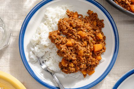 Overhead view of a white plate with a blue rim of picadillo over rice on a white table cloth
