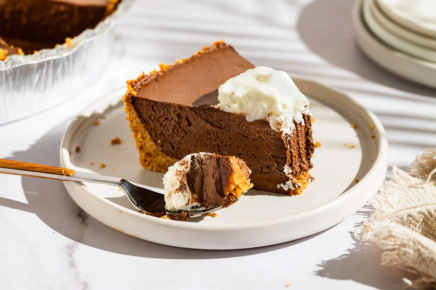 A slice of chocolate cream pie on a plate topped with whipped cream with a forkful taken out
