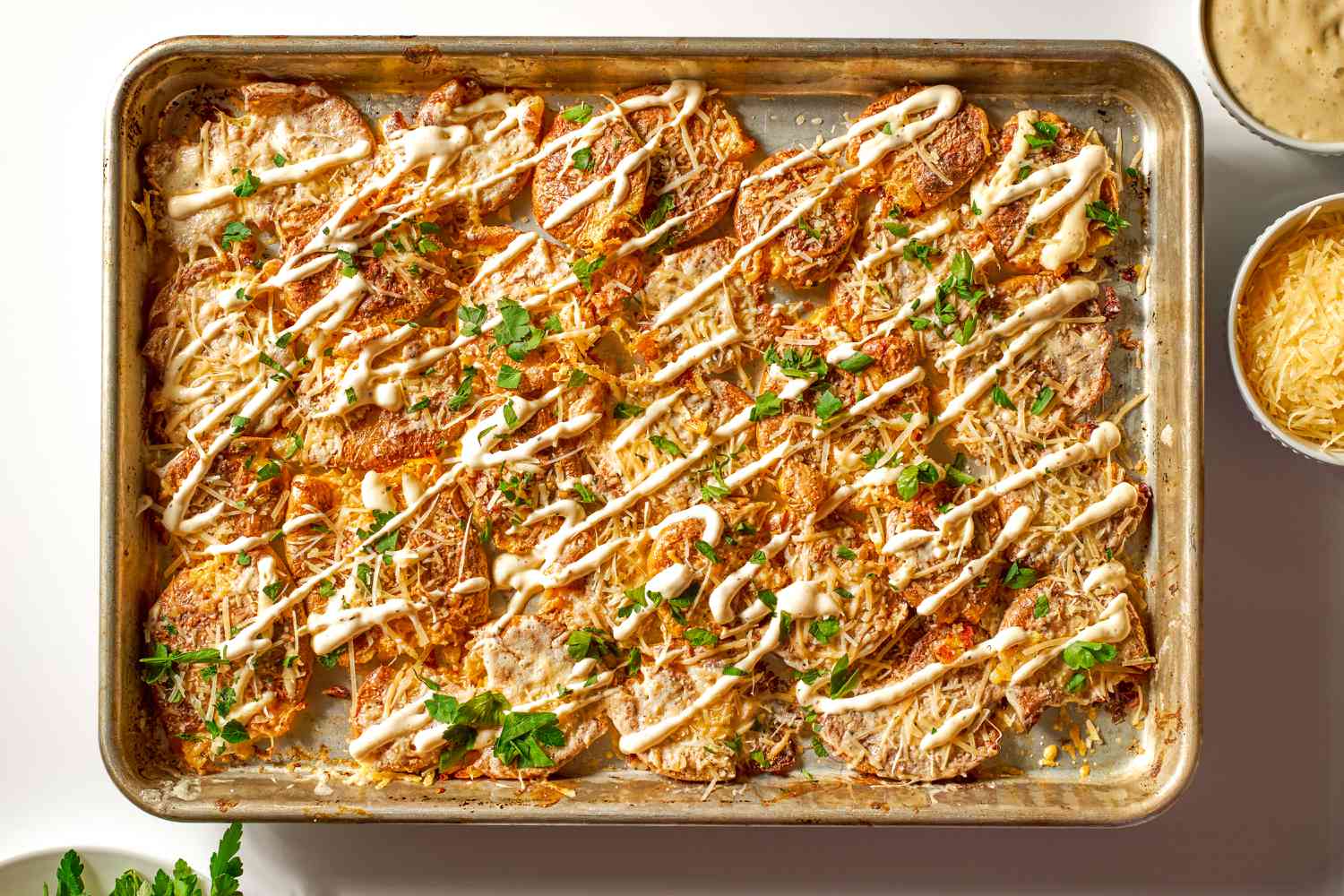 Crispy Caesar Smashed Potatoes on a sheet-pan, parmesan cheese and caesar dressing on the side
