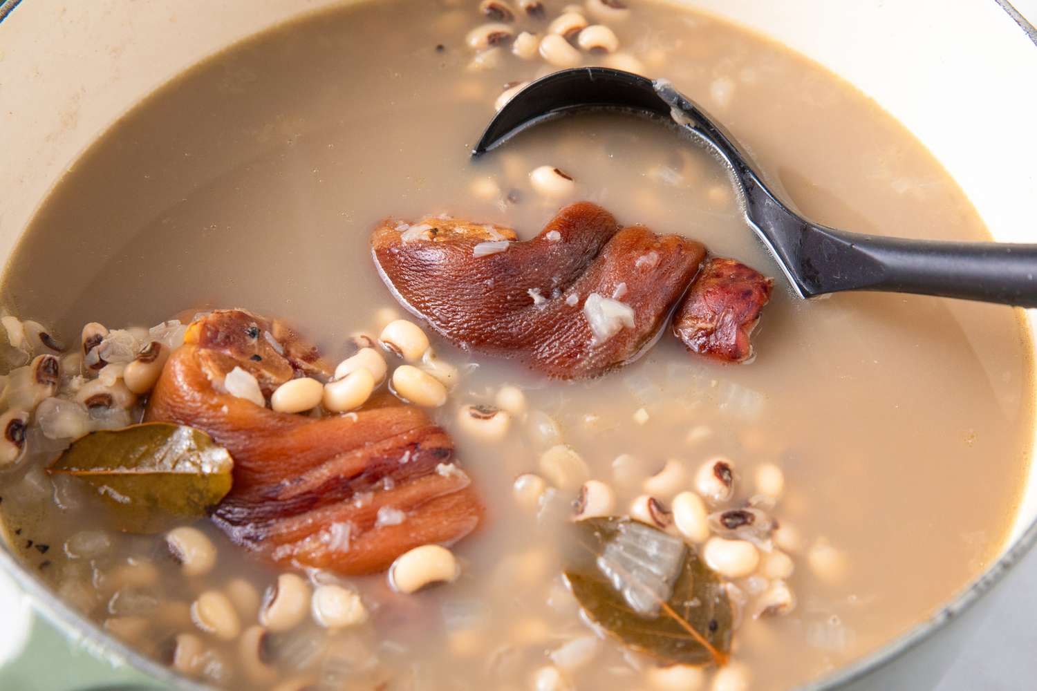 Cooked blackeyed peas with pieces of meat in a pot accompanied by a ladle