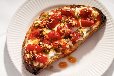 A slice of toast topped with roasted tomatoes cottage cheese and seasonings on a plate
