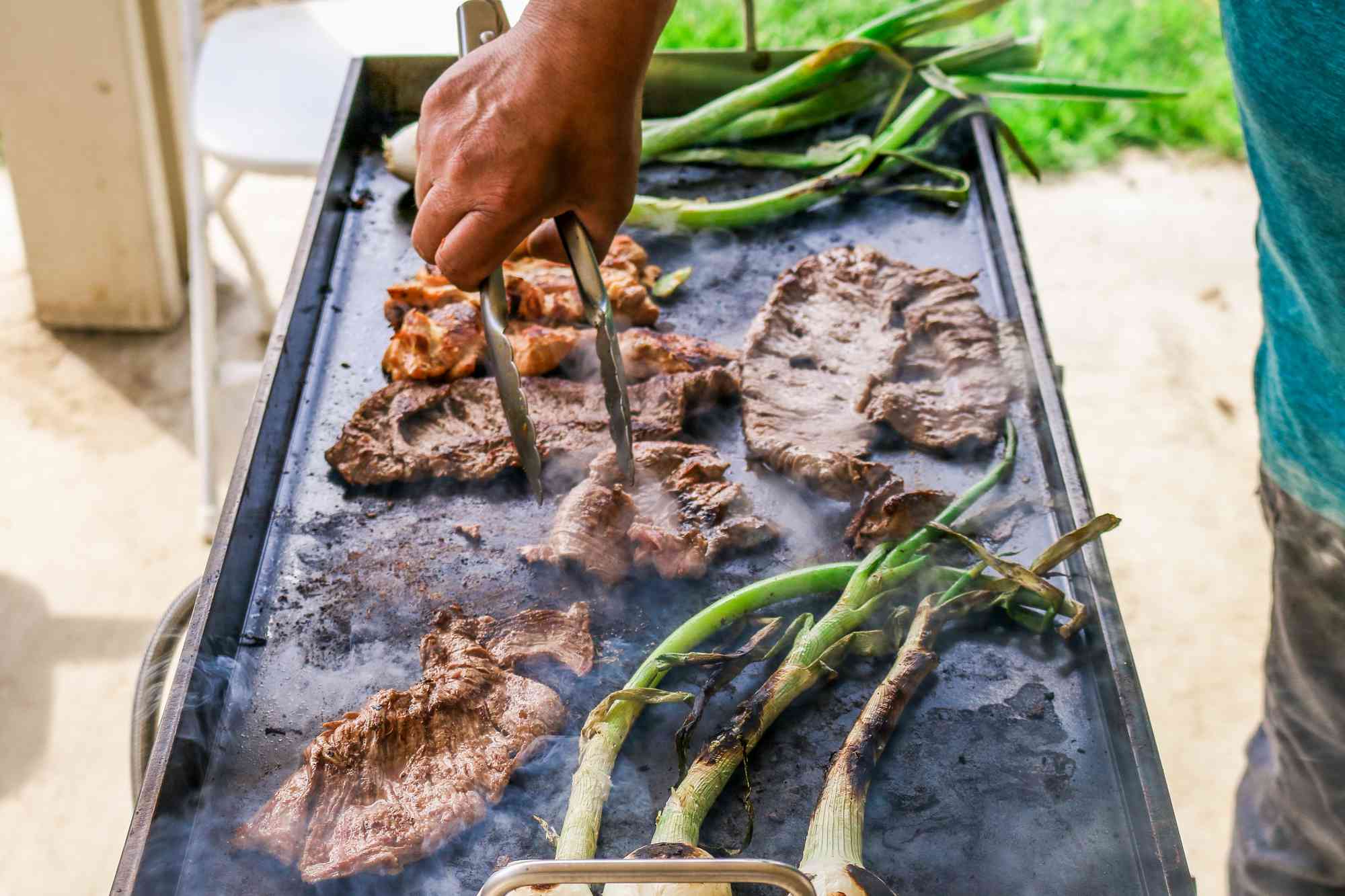 Cooking steak, chicken, and spring onions on a flat grill