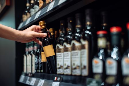 A hand reaching for a bottle of balsamic vinegar on a store shelf surrounded by other similar bottles