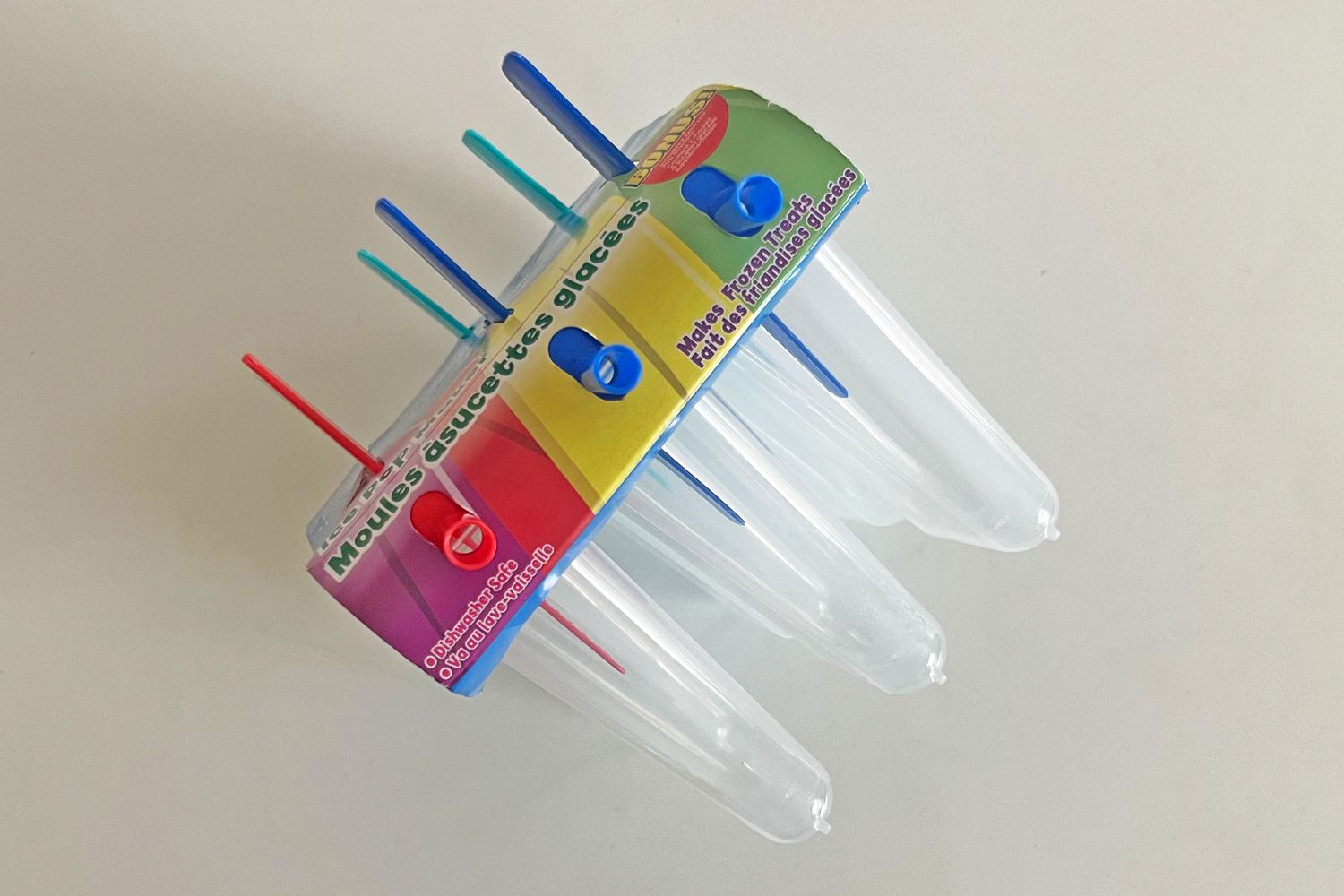 A popsicle mold with multiple clear compartments and colorful sticks, displayed on a flat surface