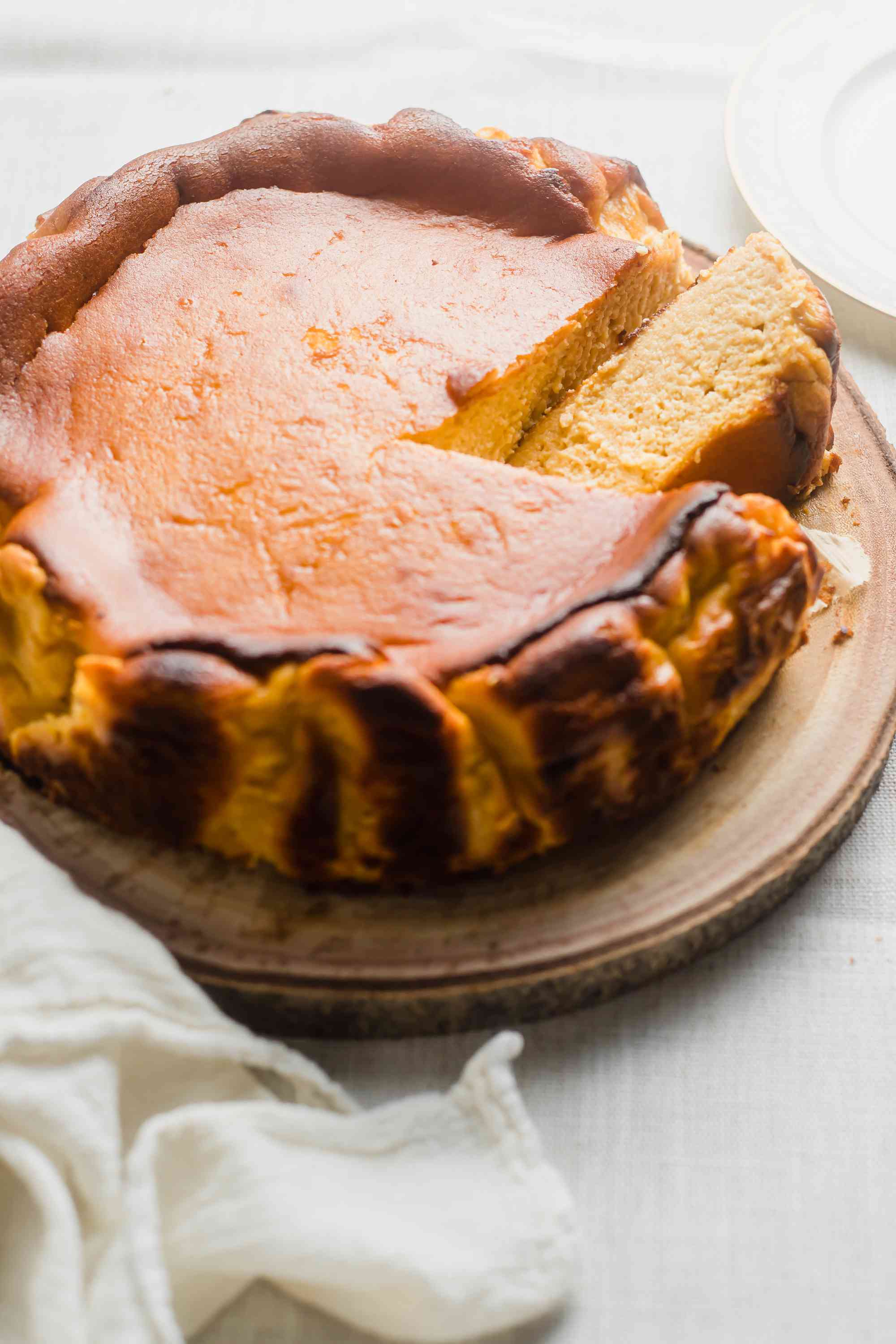 Basque Style Pumpkin Cheesecake on a wooden board with linens, one slice removed
