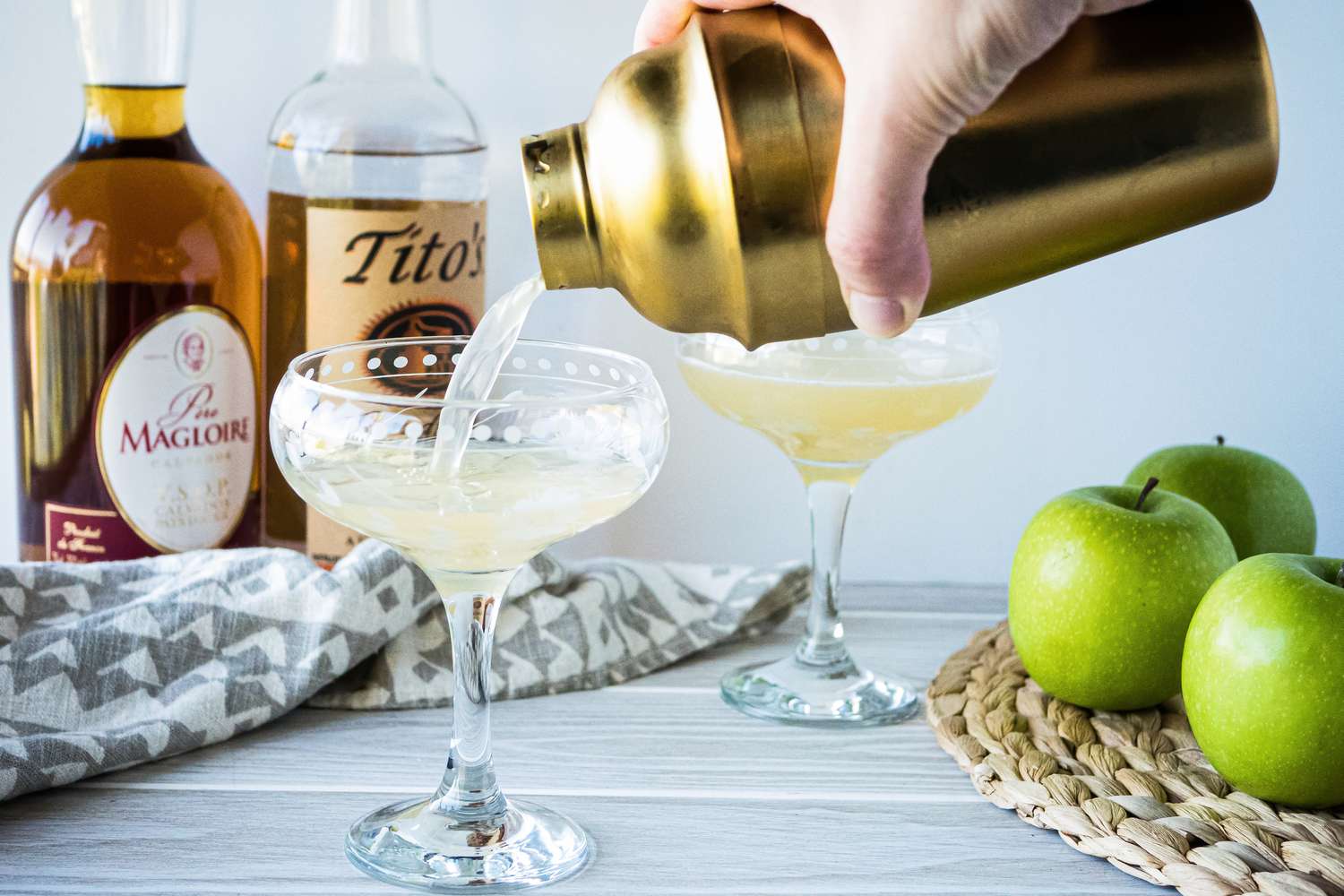 Pouring an appletini cocktail into a stemmed glass.
