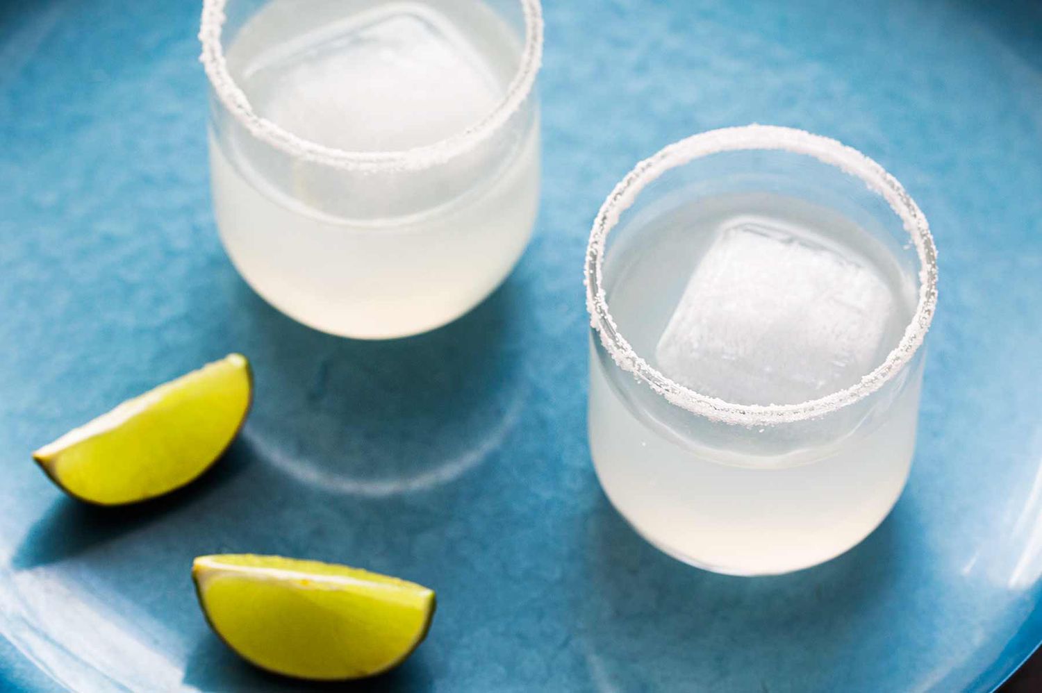 Overhead of two classic margaritas in glasses with salted rims and lime wedges off to the side