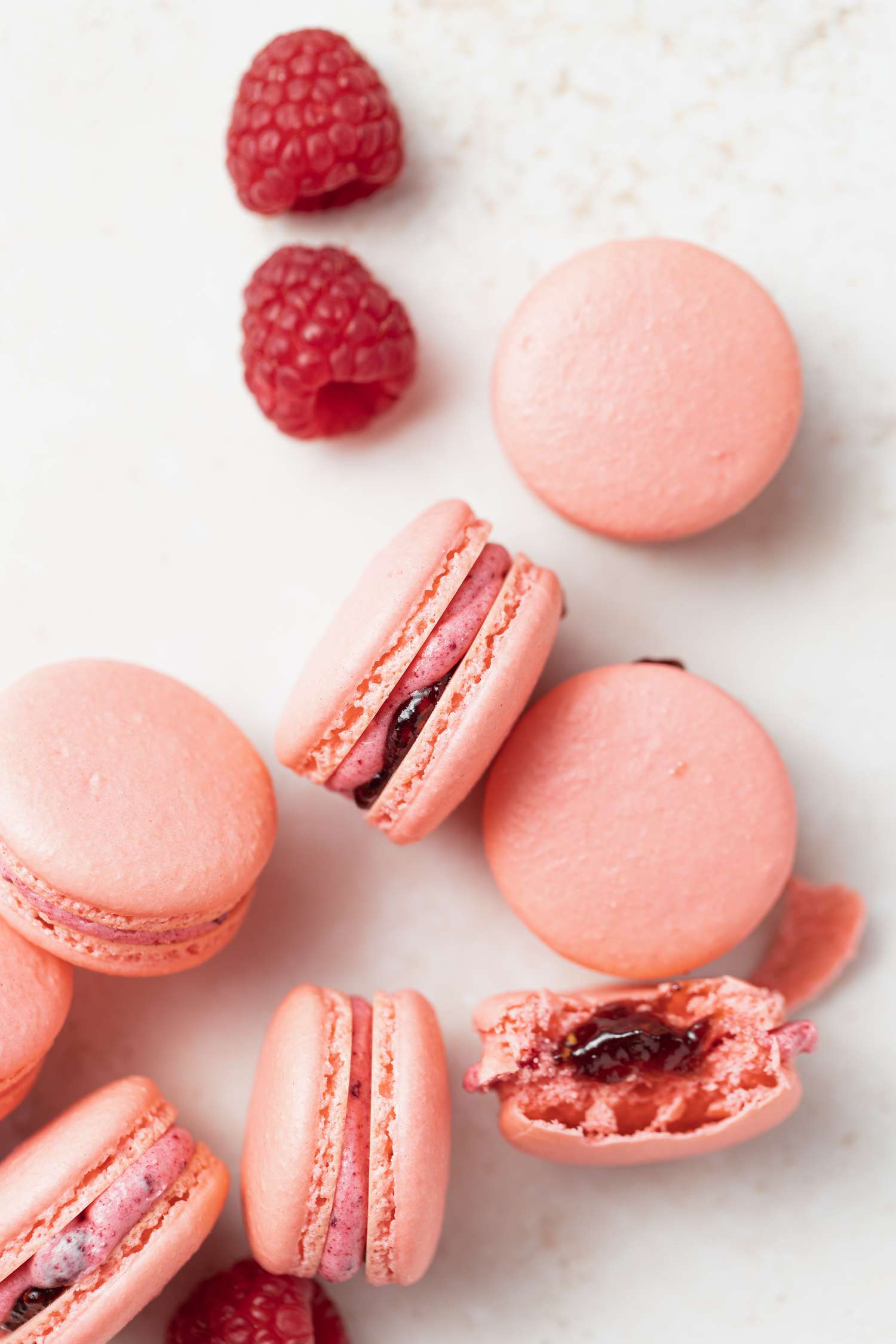 Overhead view of French macarons with raspberry buttercream filling and whole raspberries next to them.
