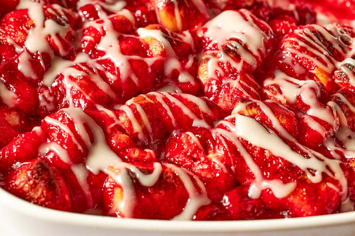 Side view closeup of cherry cobbler in a baking dish, drizzled with a glaze