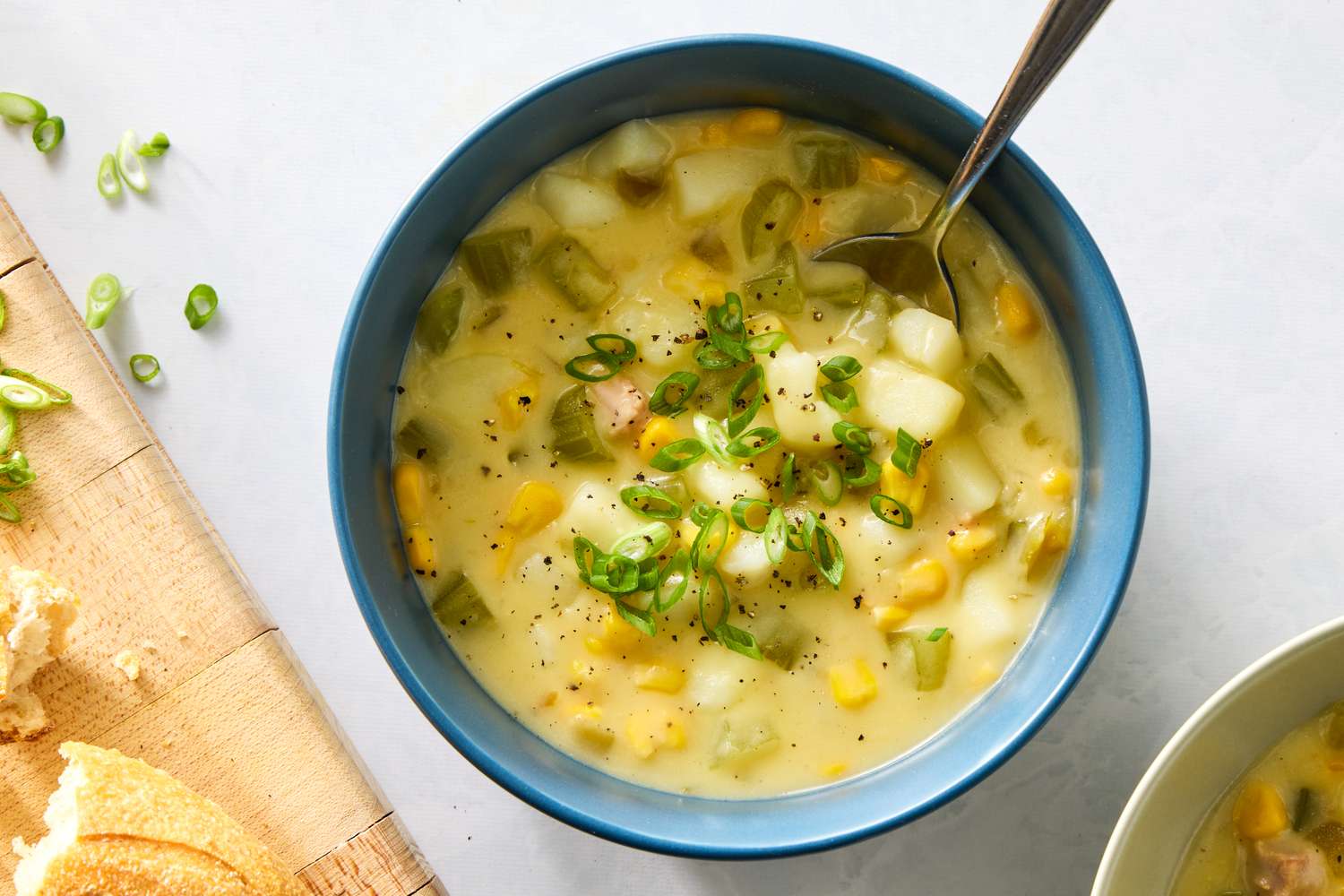 A bowl of chicken and corn chowder garnished with chopped green onions with bread slices nearby
