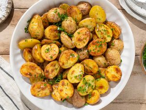 Roasted halved potatoes in a large white serving bowl, sprinkled with flakey salt and parsley