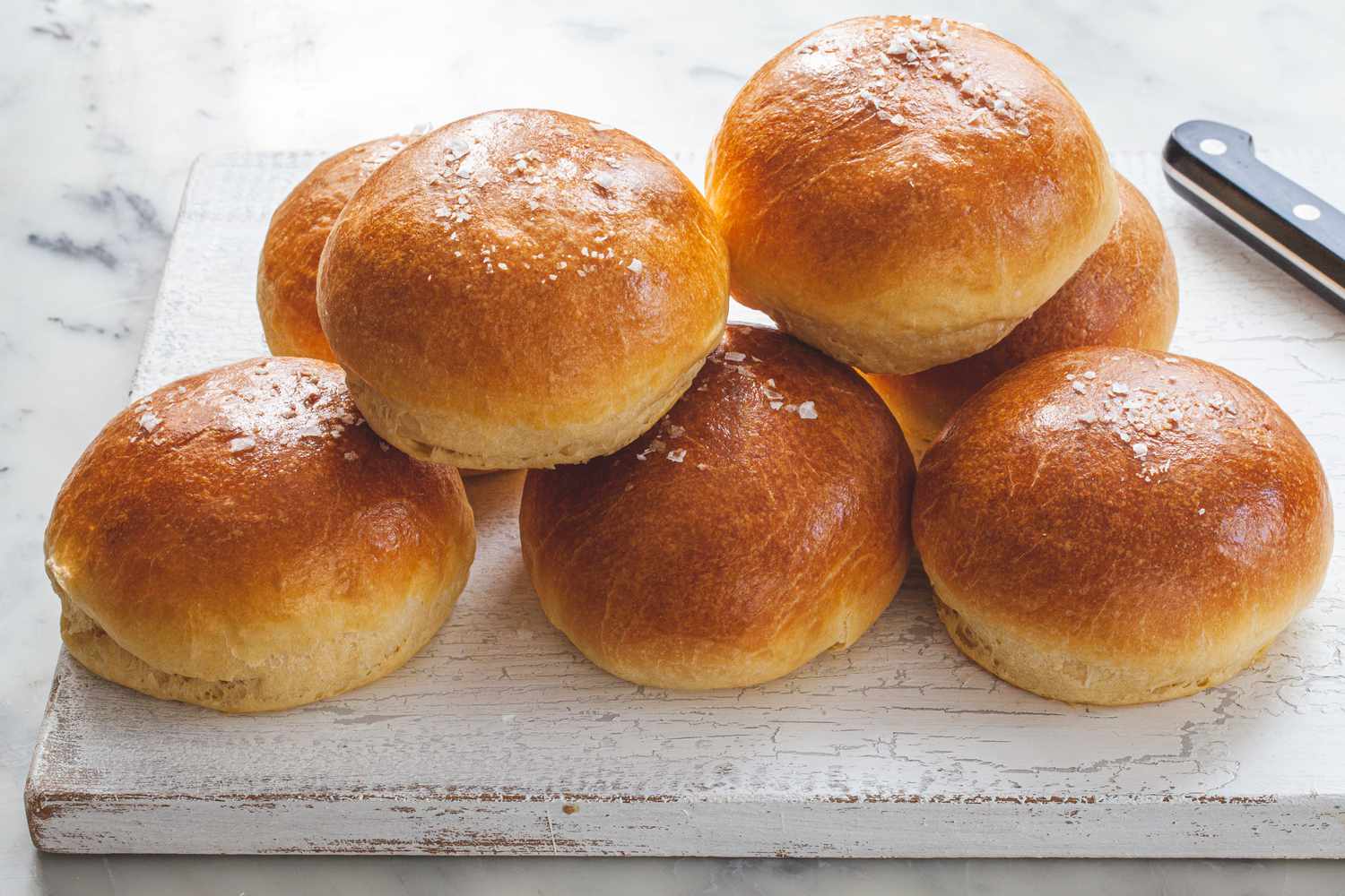 The Fluffiest Brioche Buns stacked on a wood slab.