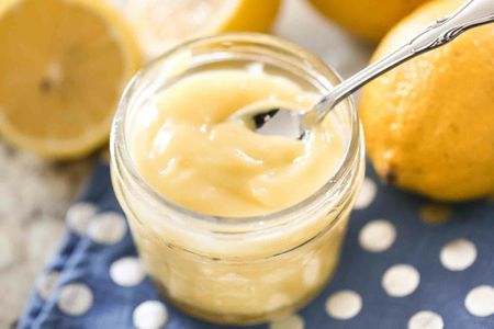Lemon curd in a jar with a spoon and lemons in the background