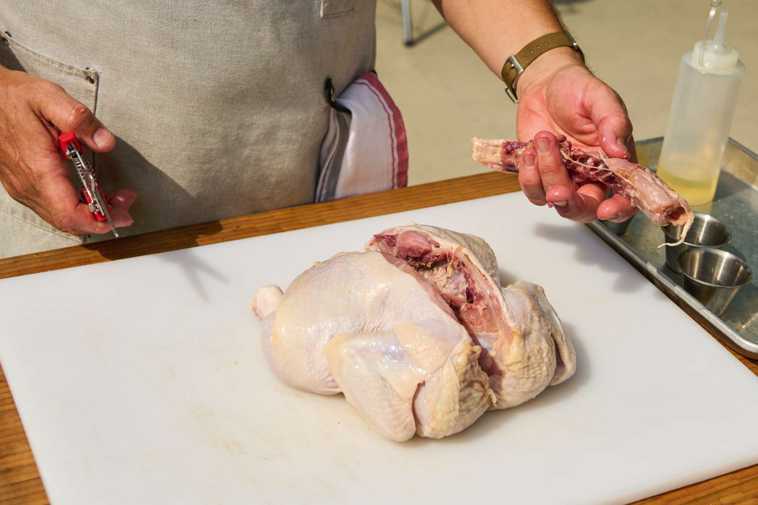 Preparing a raw chicken by removing bone on a cutting board for Grilled Half Chicken recipe