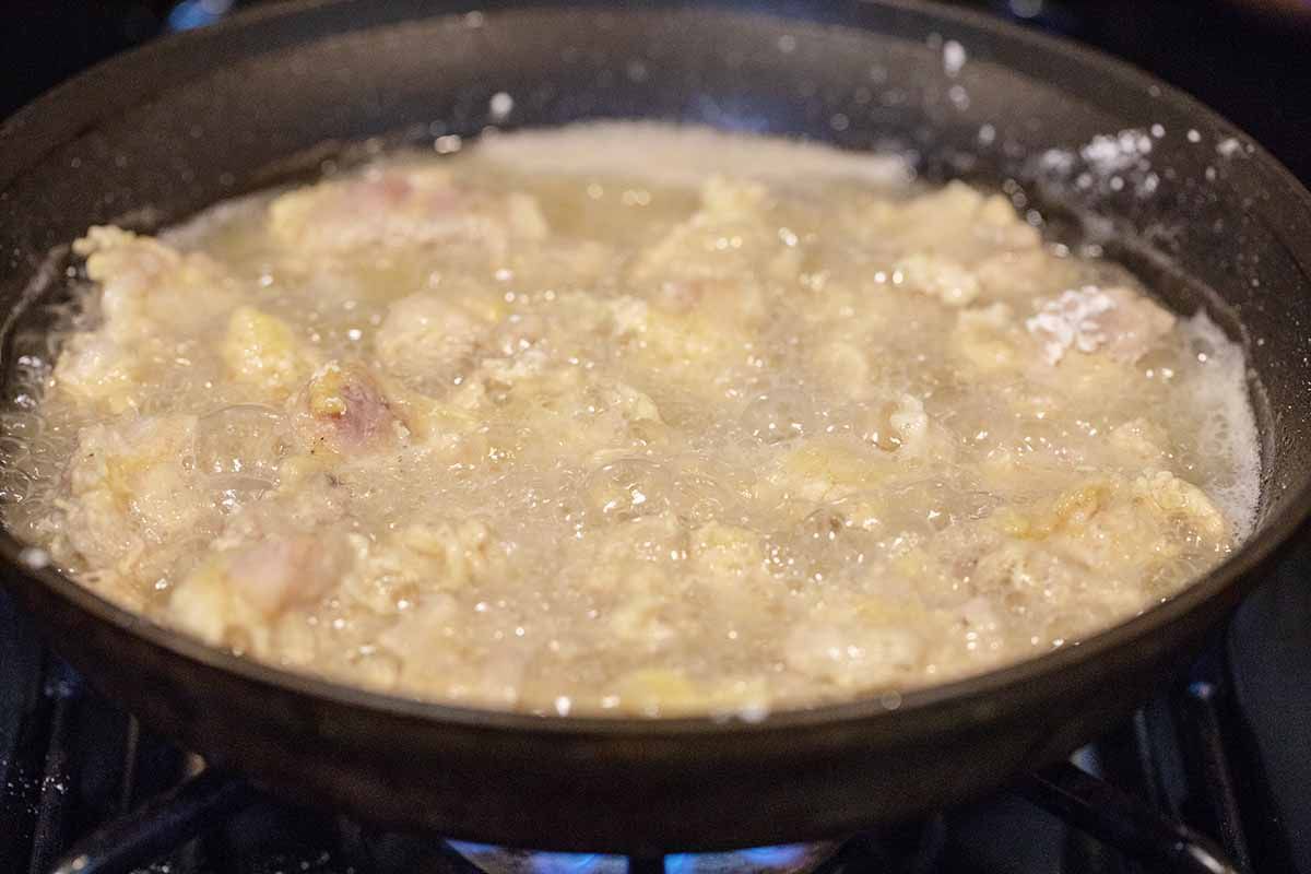 Side view of chopped chicken frying in a cast iron skillet.