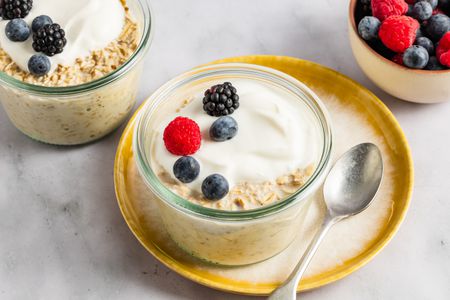 Two glass ramekins with overnight oats, topped with fresh berries, with a small bowl of berries in the background