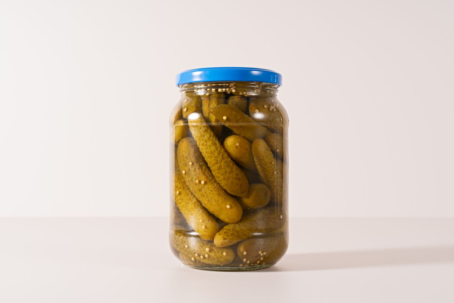 A transparent jar filled with pickles and sealed with a blue lid