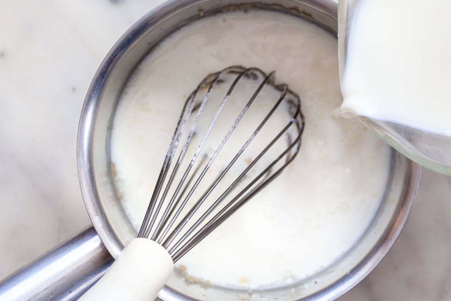 Whisking white sauce or béchamel sauce in a saucepan.
