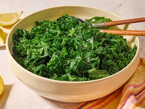Angled view of a large bowl of kale salad with serving spoons next to lemon slices and a cloth napkin