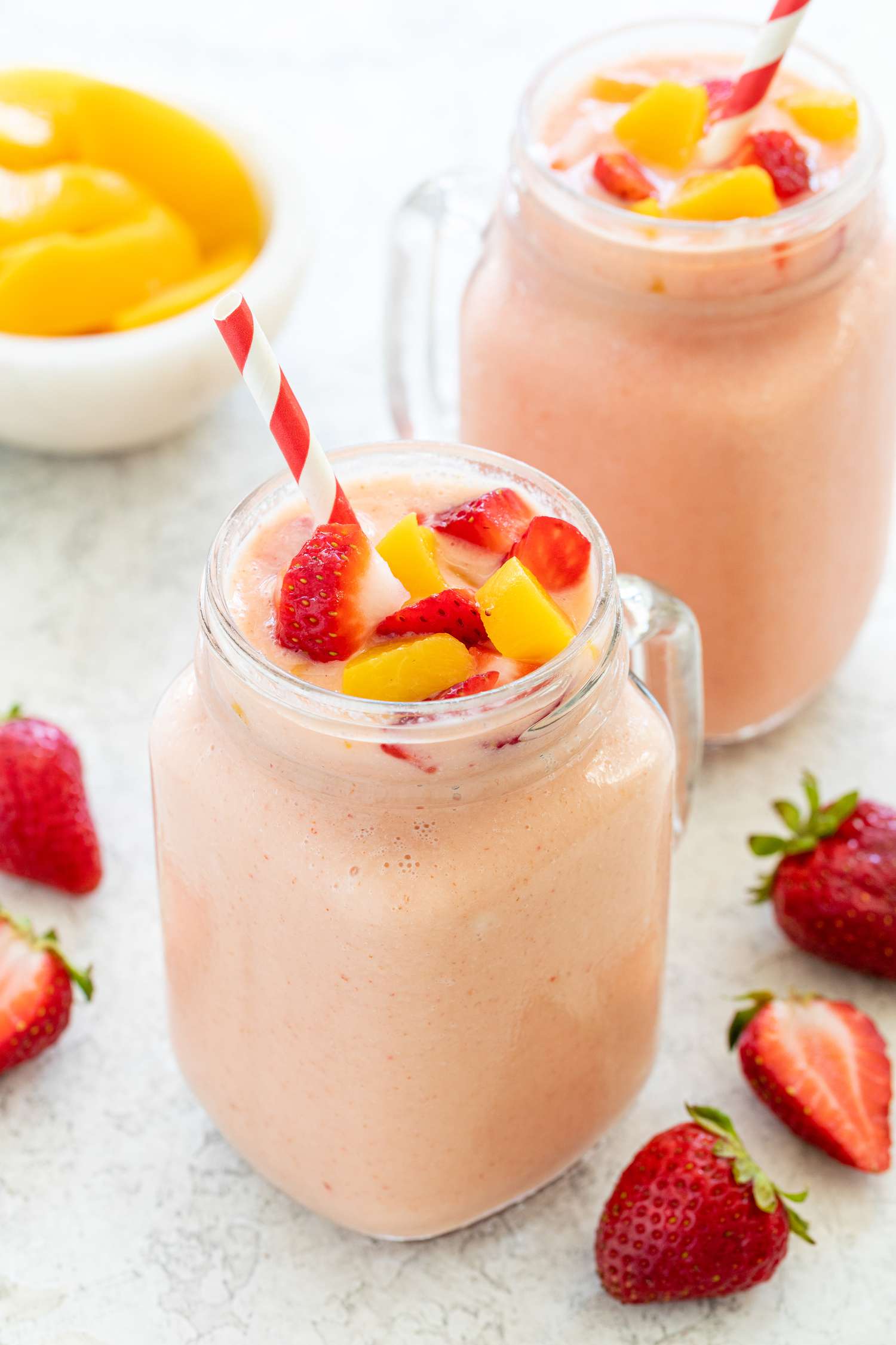 Two strawberry peach smoothies with Greek yogurt in a mason jar with fresh fruit around it.