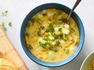 A bowl of chicken and corn chowder garnished with chopped green onions with bread slices nearby