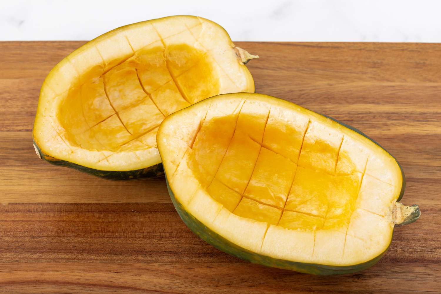 Seeded acorn squash with hash marks cut into the flesh.