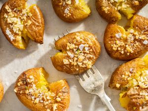 Roasted smashed potatoes topped with crushed nuts on a baking surface with a fork