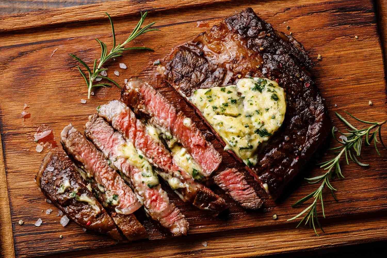 Sliced grilled steak topped with butter served on a wooden board with garnishing