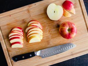 Sliced and whole apples on a cutting board with a knife placed nearby