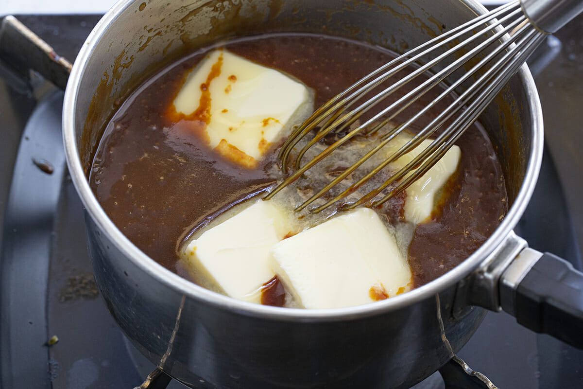 Butter being whisked into a pot of caramelized sugar to make caramel sauce.
