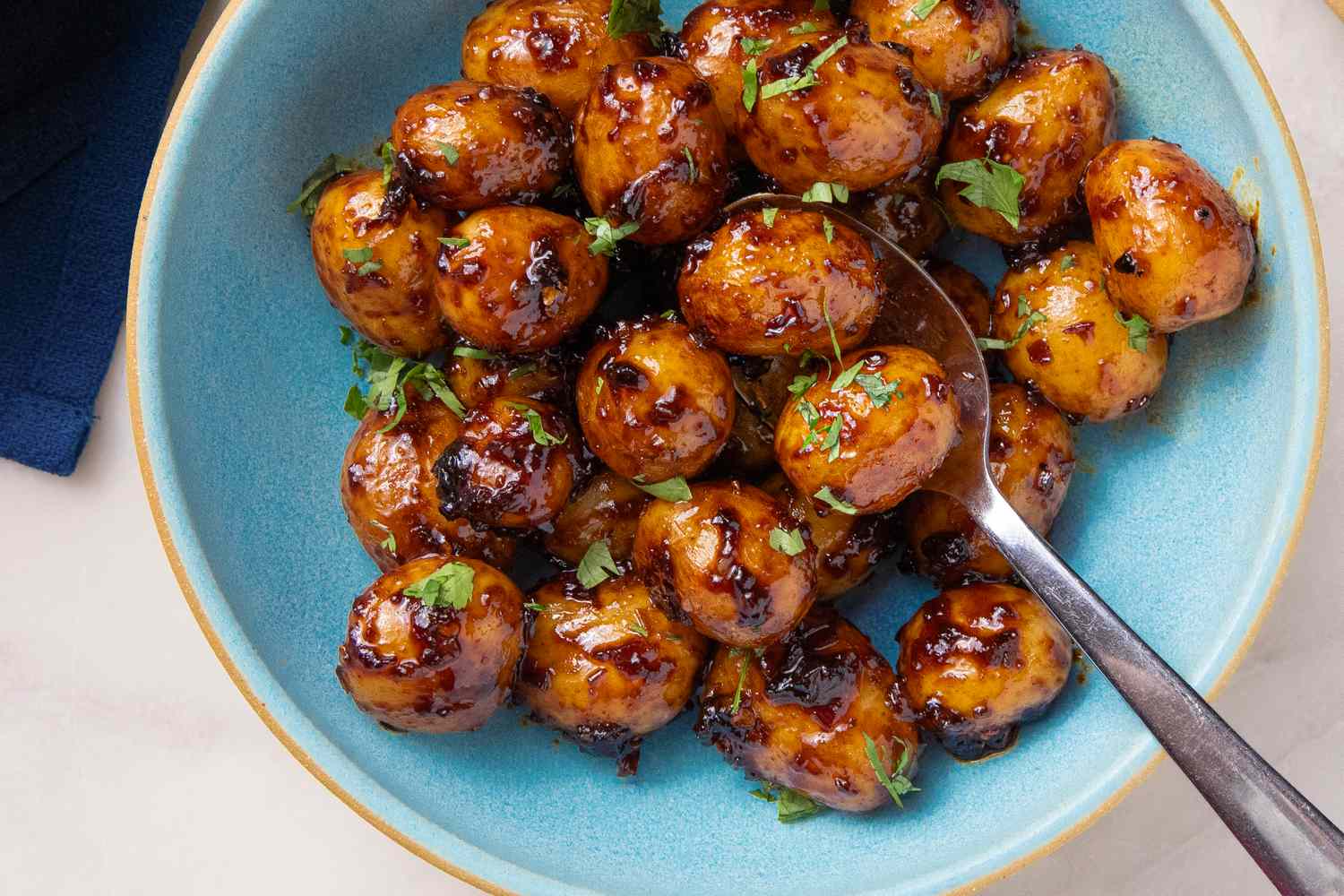 A bowl of Southwestern sticky potatoes coated in a saucy glaze with chopped herbs served with a spoon
