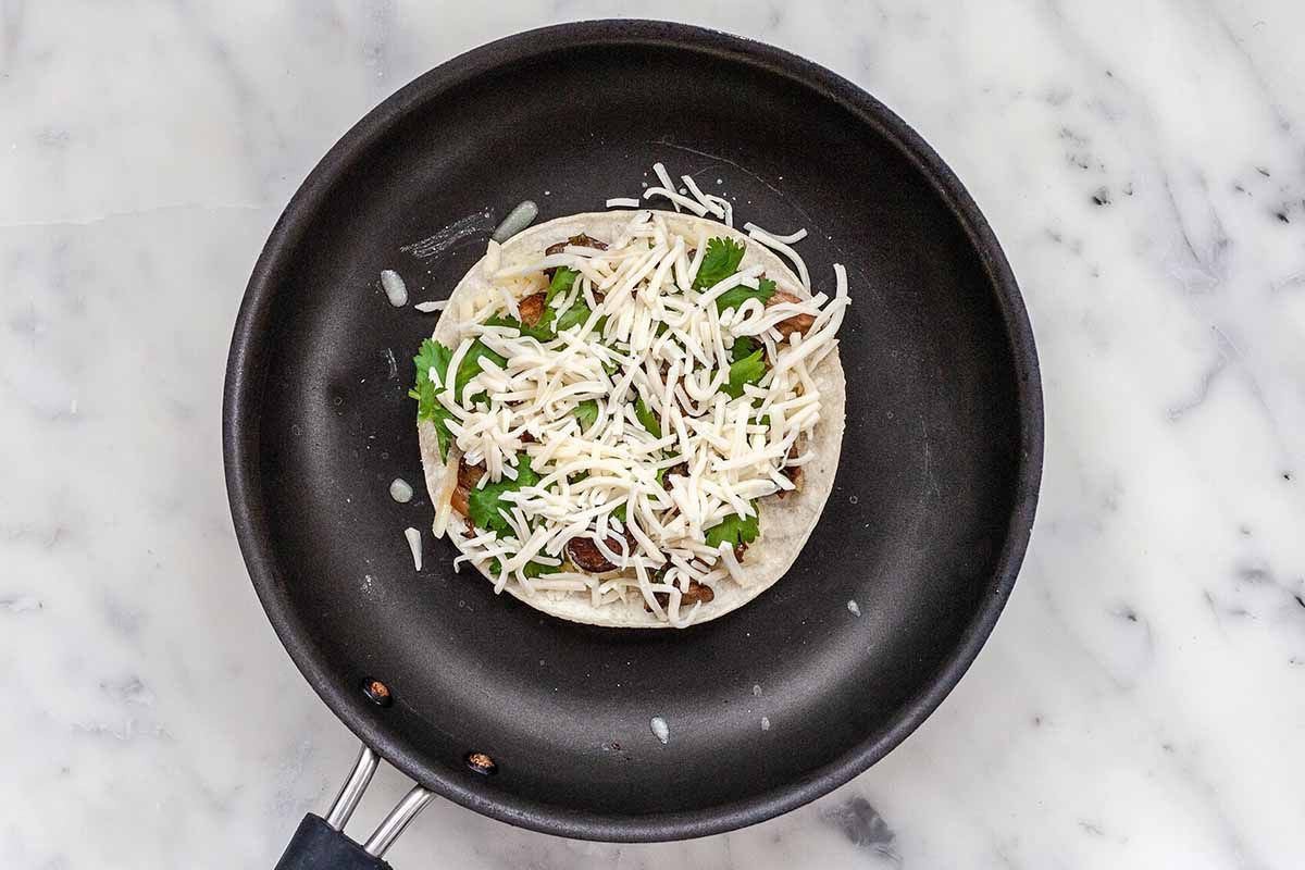 Quesadilla Recipe with Cheese and Mushrooms - tortilla in black skilled. Cheese, musrooms and cilantro are ontop of the tortilla