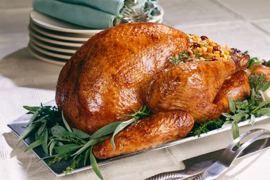 A whole roasted turkey on a serving plate, with herbs around it as decoration