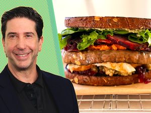 David Schwimmer next to a sandwich filled with assorted ingredients placed on a wire rack