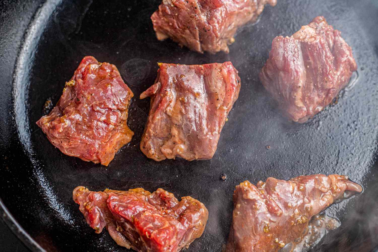 Steak tips cooking on a hot cast iron skillet