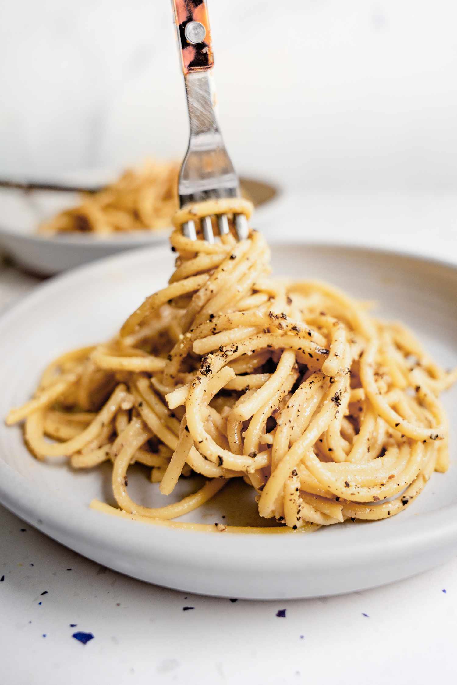 Vegan Cacio e Pepe Topped with Cracked Pepper on Plate with Some of Pasta Wrapped around a Fork
