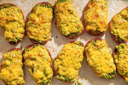 Broccoli and cheddar cheese toasts arranged in rows on a baking sheet