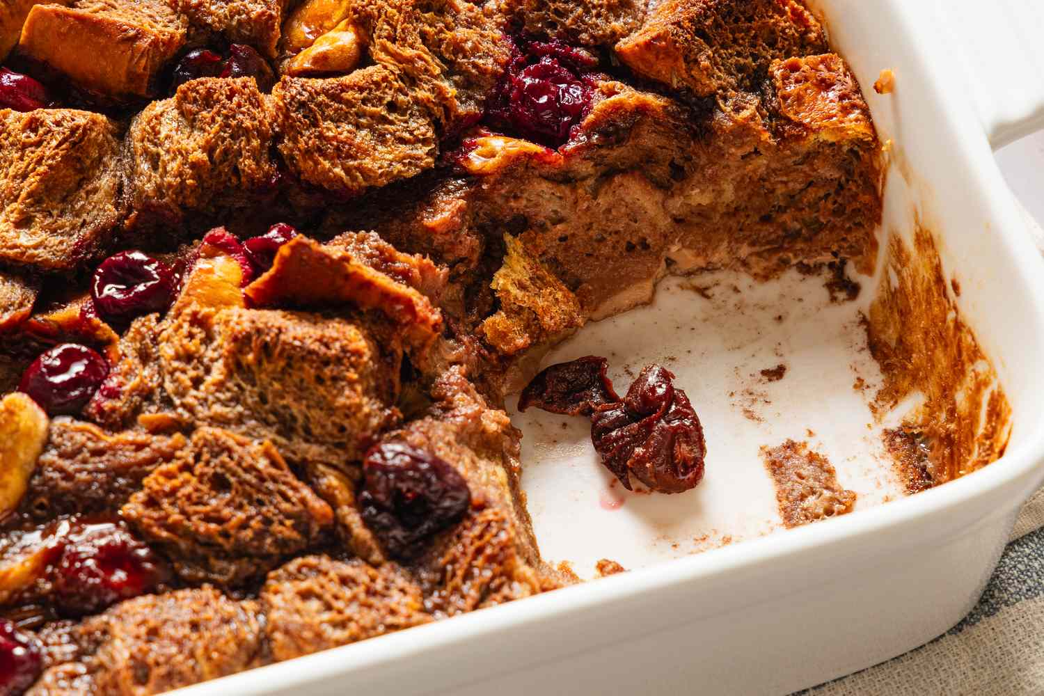 A casserole dish containing Nutella and cherry French toast bake is partially served with cherries visible on top