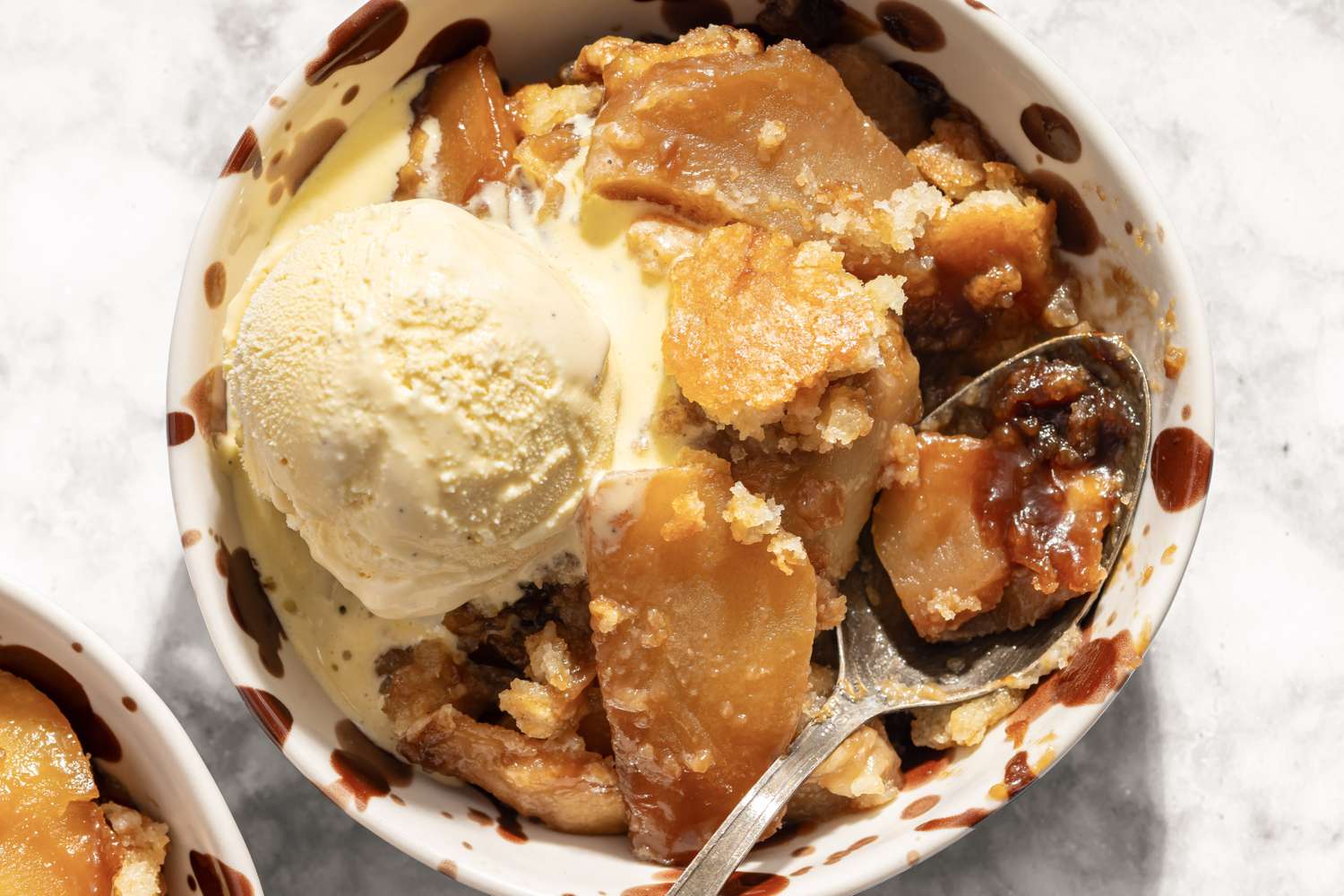 Closeup view of a serving of caramel apple cobbler topped with a scoop of vanilla ice cream in a bowl