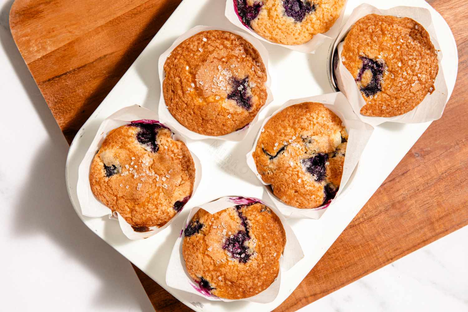 A tray of baked blueberry muffins lined with paper wrappers