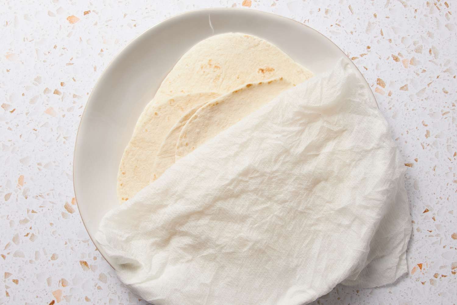 Flour Tortillas on a Plate Partially Covered in a Wet Paper Towel