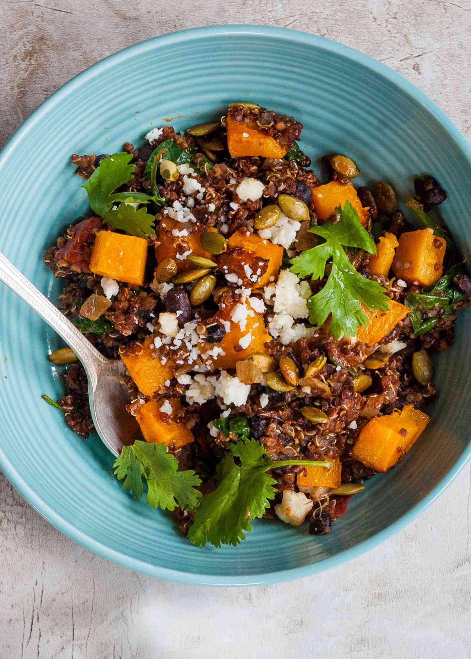 A blue bowl with mexican-style black bean skillet dinner and a spoon resting in it.