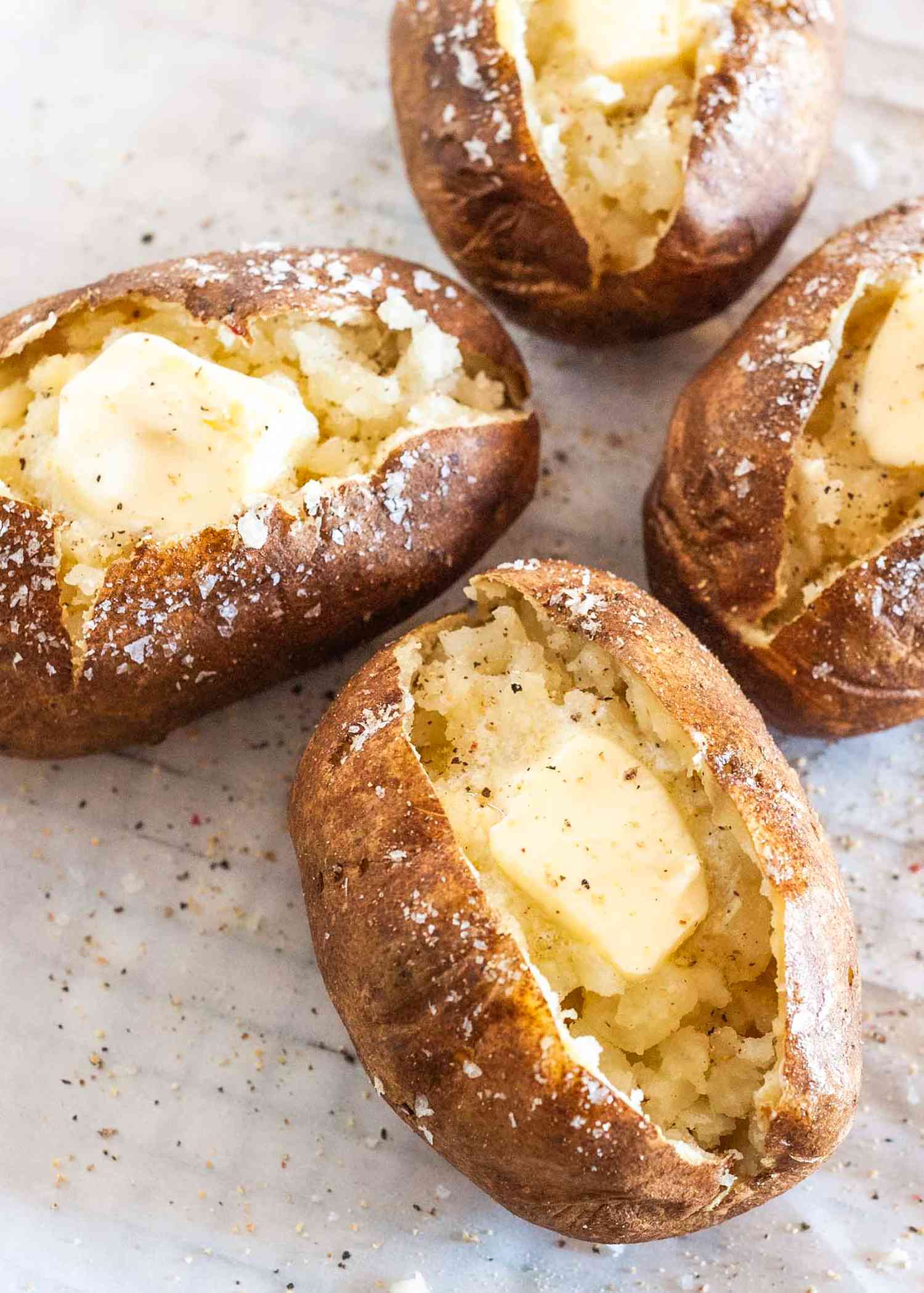 Baked potatoes on a parchment paper lined wire rack (potatoes served with flaky salt, pepper, and butter)