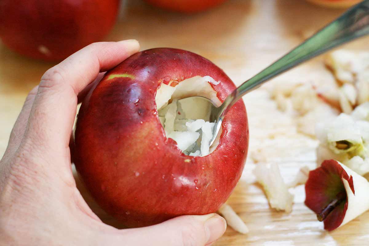 Apple insides being scooped out with a spoon to make room for stuffing