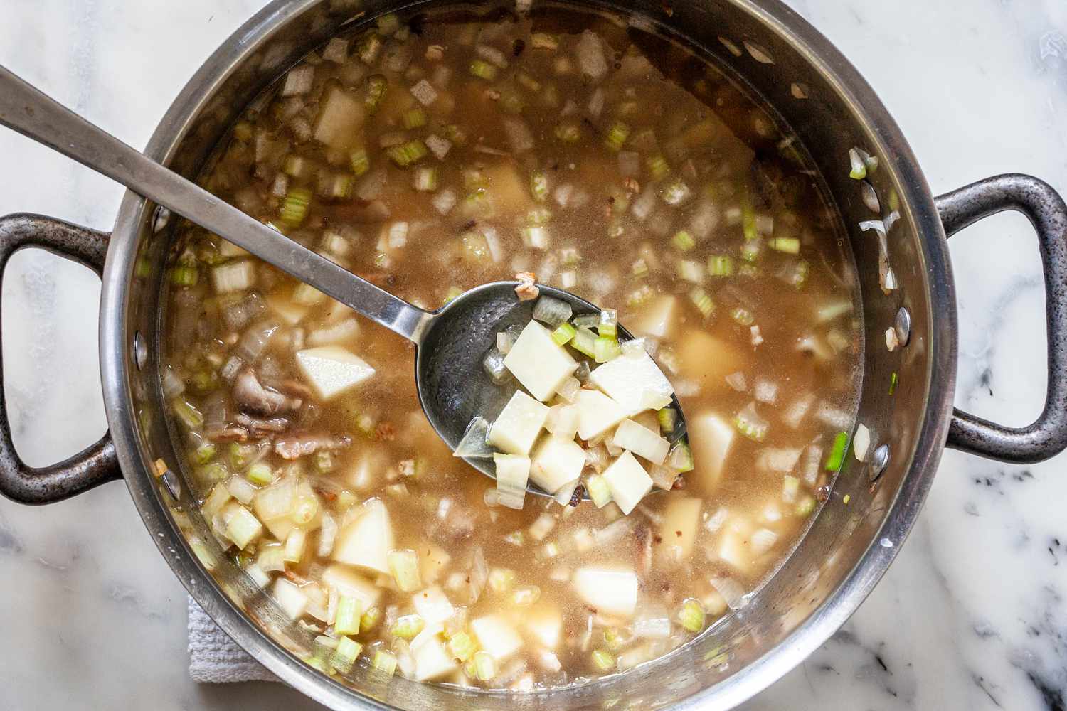 Broth and Cubed Potatoes in Pot of Classic New England Chowder with Some Potatoes Lifted from Pot Using a Spoon