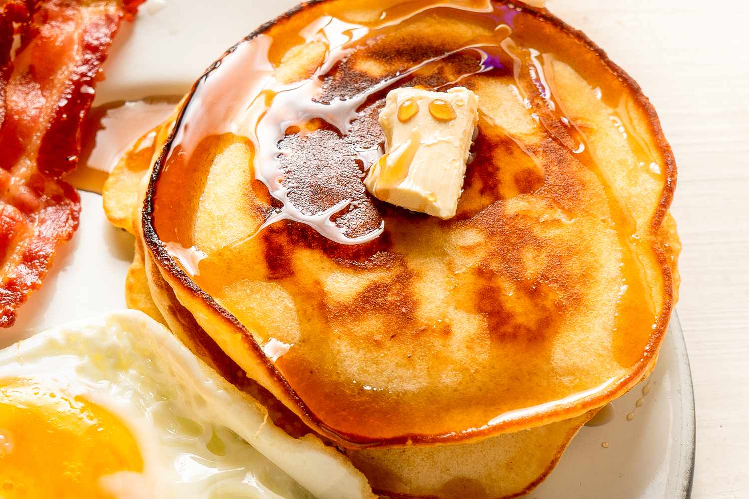 A plate with pancakes topped with butter and syrup served alongside bacon and a fried egg